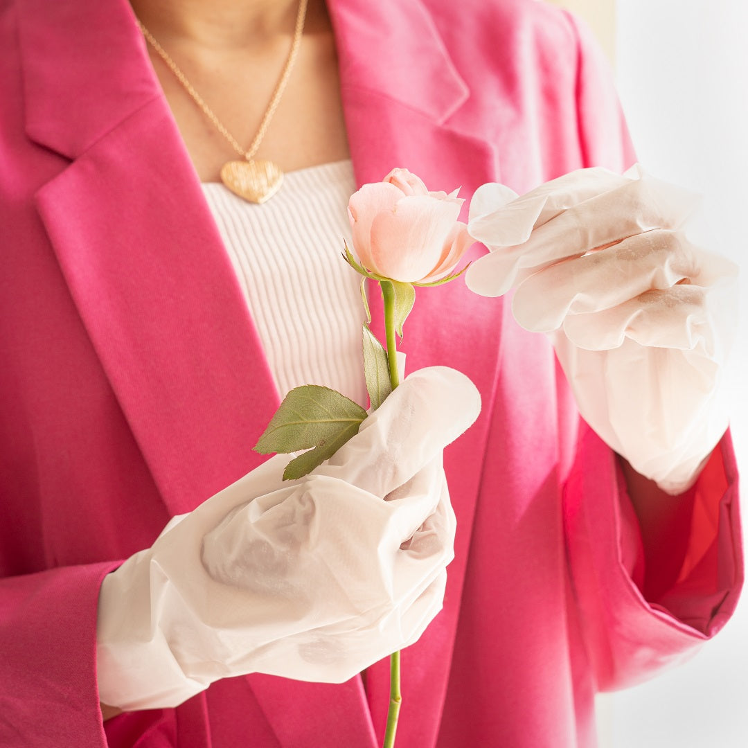 Hands wearing a white hand mask holding a pink rose.